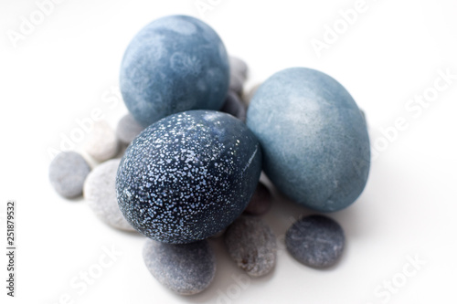 Three colored blue, gray marble eggs lie on a white background on stones