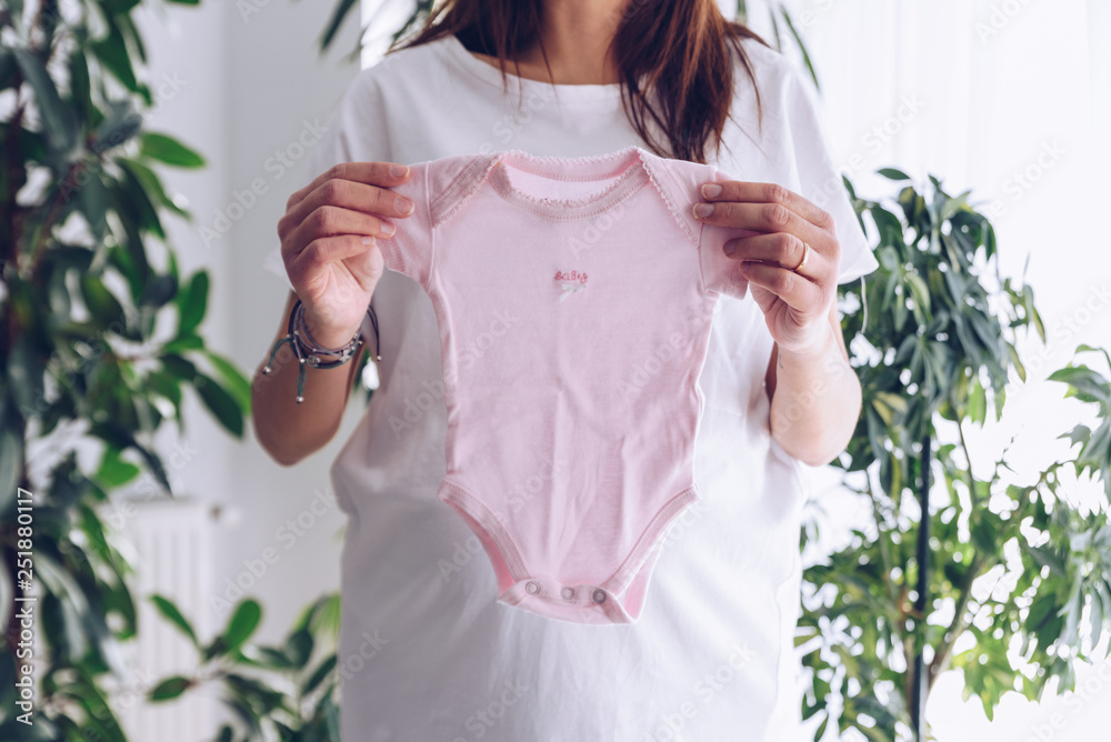 Pregnant woman holding pink baby clothes in her hands Pregnant woman holding pink baby clothes in her hands