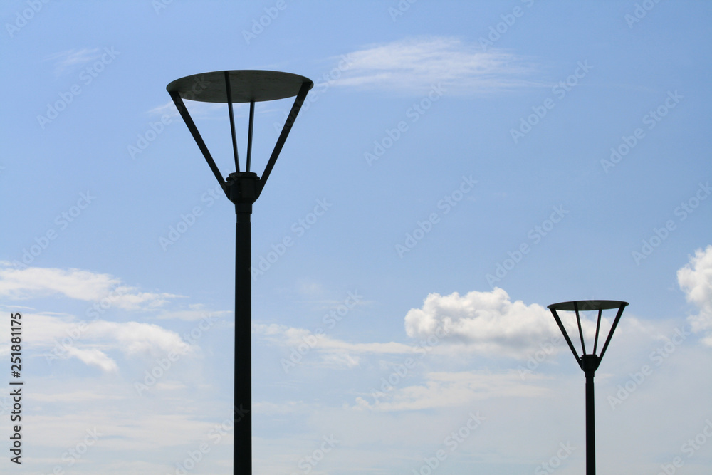 Two tall metal street lamps in front of the blue sky