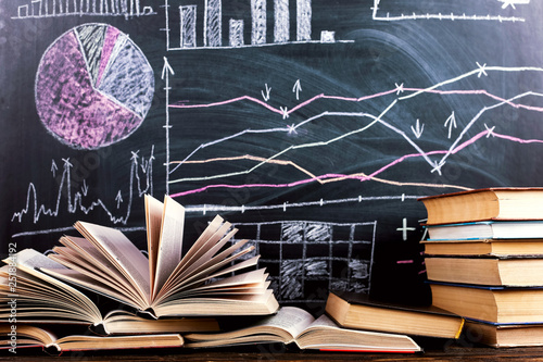 Books on the table against the background of a chalkboard on which are drawn graphs and charts of growth and decline. Business training school.
