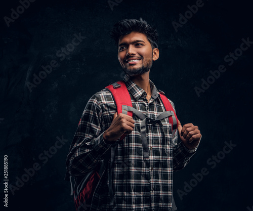 Photography Portrait of a handsome Indian student with a backpack wearing a plaid shirt, smiling and looking sideways