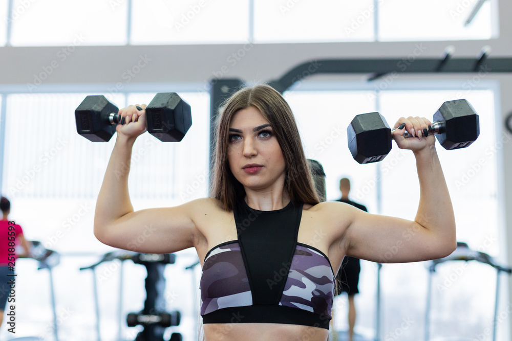 Very beautiful girl trains shoulders with dumbbells on the bench in the gym. Very beautiful girl trains shoulders with dumbbells on the bench in the gym.