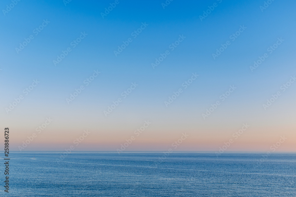 beautiful blue sky over a slightly rippling blue sea in Ramsgate, Kent with the golden haze of a late afternoon sunset hovering above the horizon