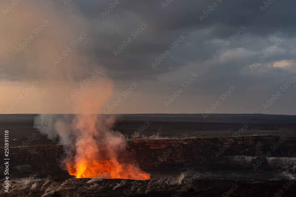 A volcanic crater at dawn. The glow and smoke from the lava is visible. It is the Kilauea volcano on Hawaii's big island.