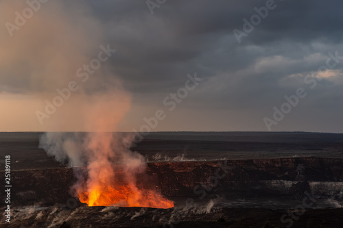 A volcanic crater at dawn. The glow and smoke from the lava is visible. It is the Kilauea volcano on Hawaii's big island.