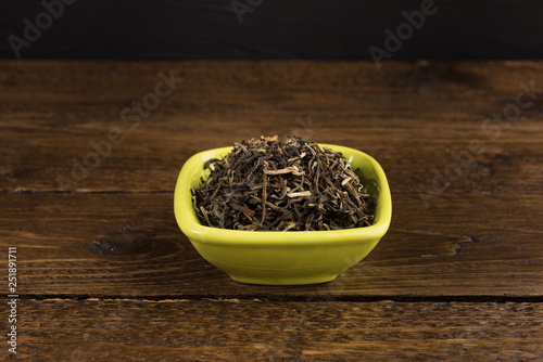 dry green tea in a clay bowl isolated on wooden table on black background