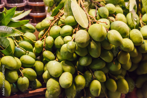 fresh wild natural tropical Asian green raw unripe mangoes juicy stone fruit  drupe  from garden on farmer market stall. Seasonal Food Nutrition  Summer mango fruit on street food market booth concept