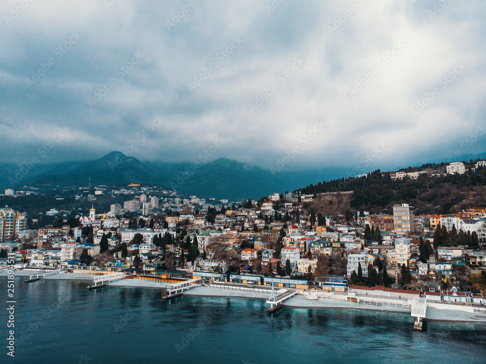 Aerial panoramic view of Yalta city embankment with sea in cloudy weather, mountains and breakwaters, beautiful resort for vacation