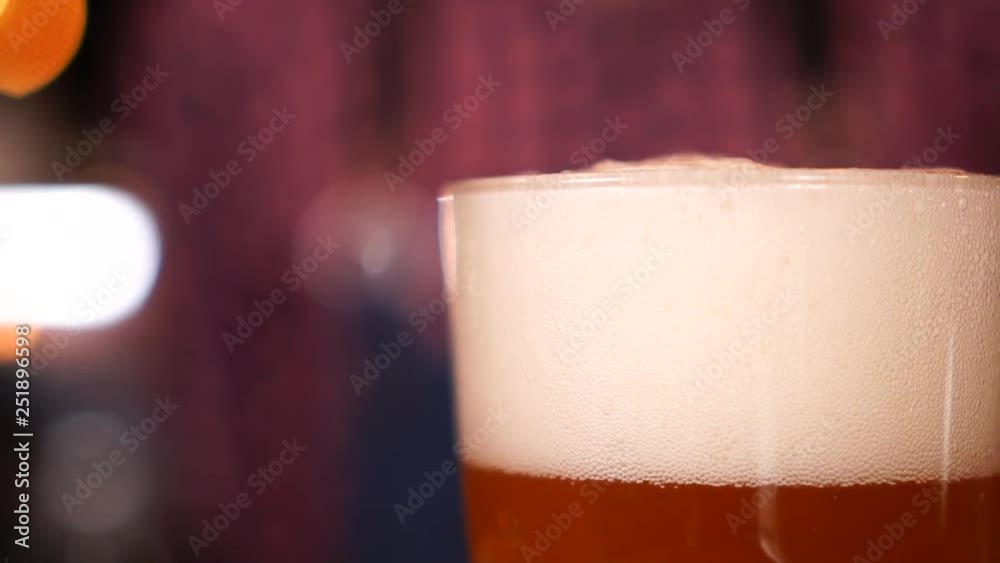 Defocused bokeh close up view on beer glass with lager pint white foam on top in slow motion Defocused bokeh close up view on beer glass with lager pint white foam on top in slow motion