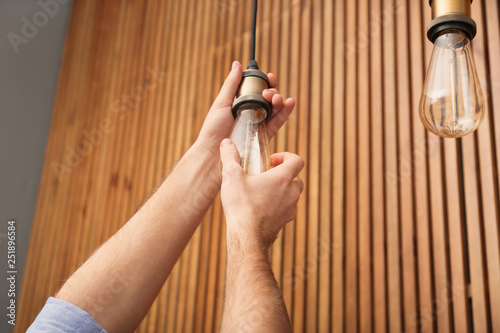 Man changing lamp light bulb indoors, closeup photo