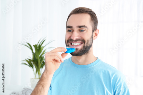 Young man using teeth whitening device at home