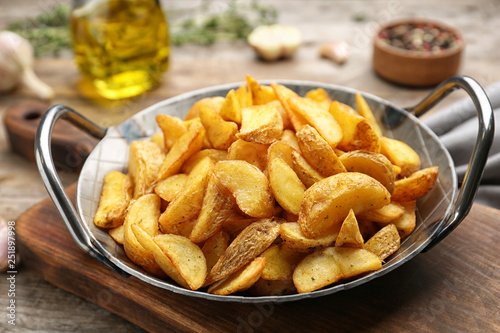 Frying pan with tasty baked potato wedges on wooden table