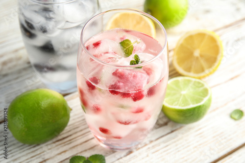 Glass of drink with pomegranate ice cubes on wooden background