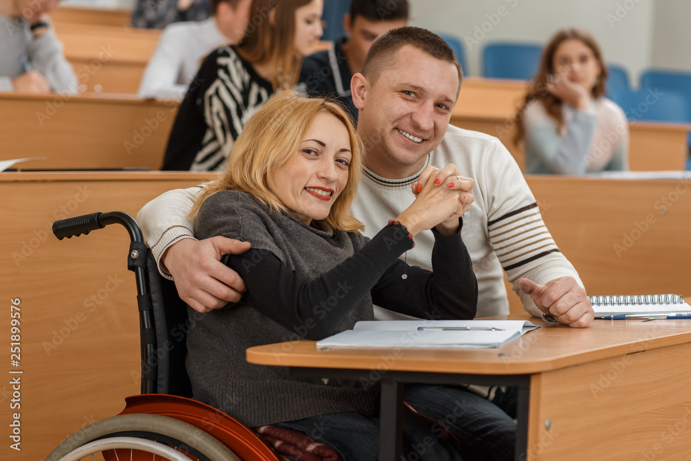 Happy students in wheelchair enjoying studying in university. Positivity man and blonde woman sitting at table, looking at camera, showing sign ok and posing. Concept of learning and ambitions. Happy students in wheelchair enjoying studying in university. Positivity man and blonde woman sitting at table, looking at camera, showing sign ok and posing. Concept of learning and ambitions.