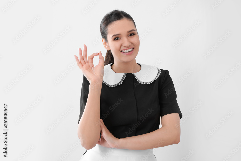 Young maid showing OK gesture on light background Young maid showing OK gesture on light background