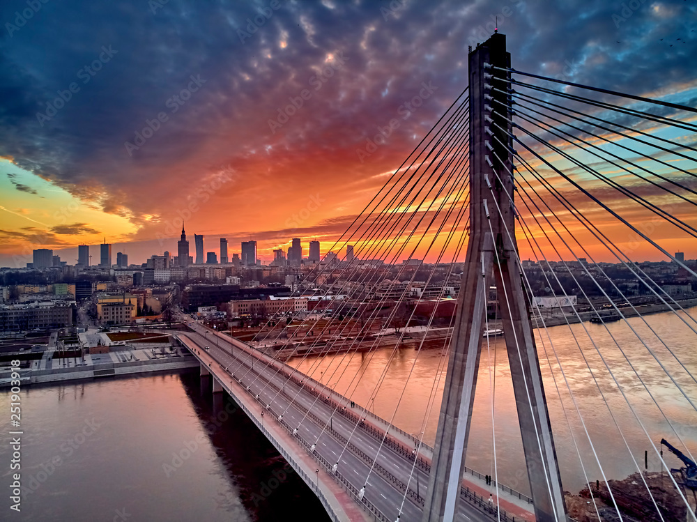 Fototapeta premium Piękny panoramiczny dron z lotu ptaka widok na zachód słońca do centrum Warszawy z drapaczami chmur i Mostem Świętokrzyskim (En: Holy Cross Bridge) - jest mostem wiszącym nad Wisłą w Warszawie