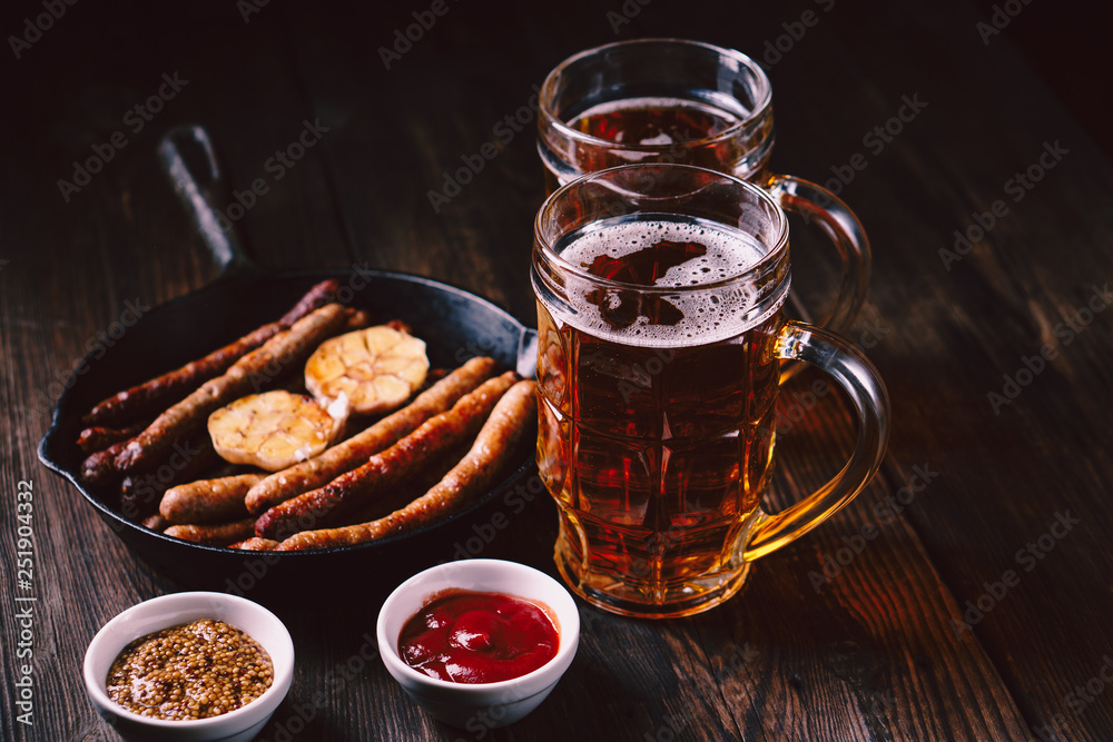beer and appetizing snacks. table with two mugs of craft lager and frying pan with homemade grilled sausages. oktoberfest food, pub concept beer and appetizing snacks. table with two mugs of craft lager and frying pan with homemade grilled sausages. oktoberfest food, pub concept