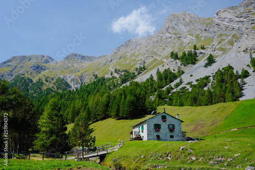 Rural house built in Italian mountain architecture style under the mountain peak surrounded by green meadows