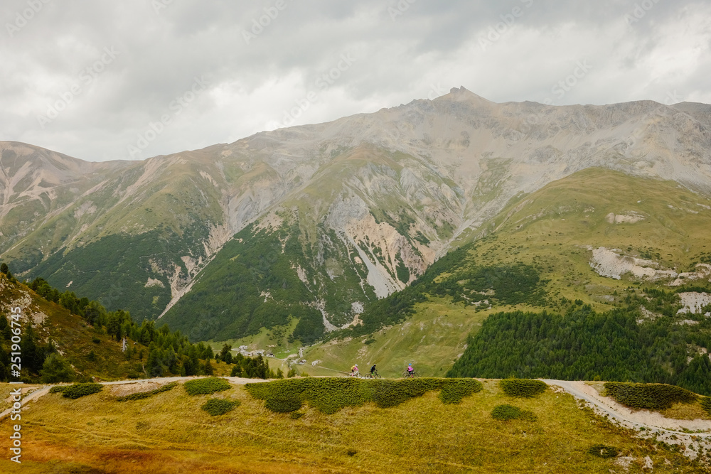 Bikers in the distance on high alpine mountain bike trail surrouned by mountains in Livigno Italy