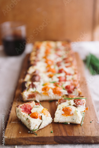 Homemade pie ( quiche) with ricotta, fresh colored tomatoes ,rectangular shapes on a cutboard,cut in cube with a wine glass,  frontal view, wooden rustic background