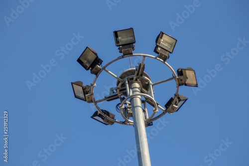 A large electric pole filled with spotlights in the blue sky