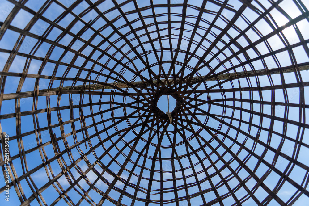 View from bottom of Traditional fishing cage made from bamboo with blue sky in background.