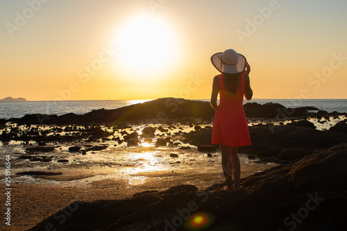 girl in a hat strolls along the beach at sunset