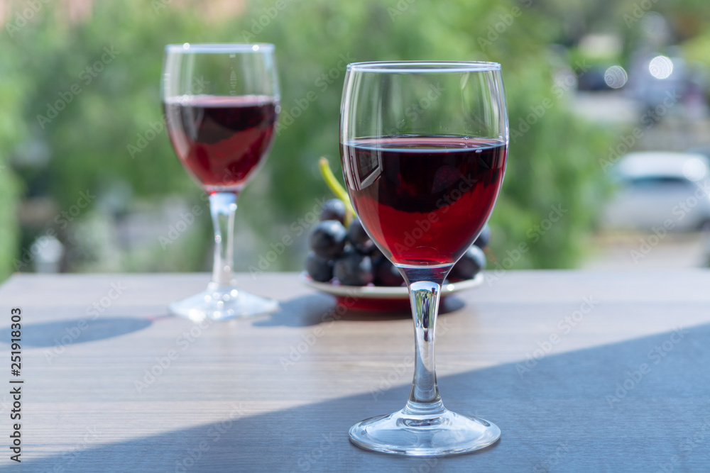 Two wine glasses with red wine served with red grape on outdoor terrace