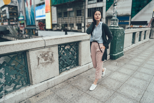 full length of young asian office lady walking on overpass wearing smart casual suit going to work in the morning. elegant japanese woman on dotonbori nipponbashi bridge outdoor looking aside relax