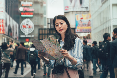vintage picture young chinese woman traveler with paper map in hands. Stylish girl with camera and backpack standing on the city street. The concept of sightseeing and urban tourism osaka japan.