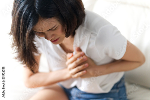 фотографія Unwell condition and sickness concept; Asian woman having heart attack sitting on sofa