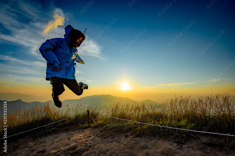 Woman jumping with fun action during sunrise at Sanknokwua (San Knok Wua) hill at Khao Laem National Park, Kanchanaburi, Thailand. Abstract of fun and Peaceful with natural clear sky background