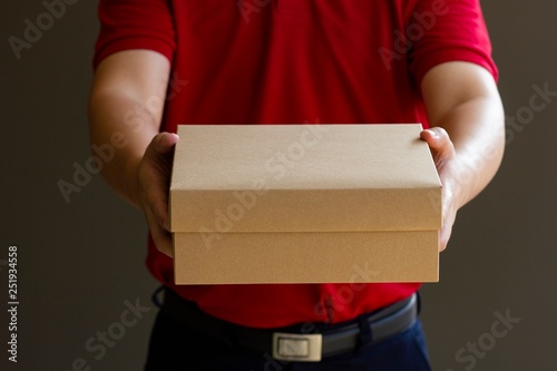 Delivery man standing with parcel post box on brown background.The delivery service concept © Patcharin