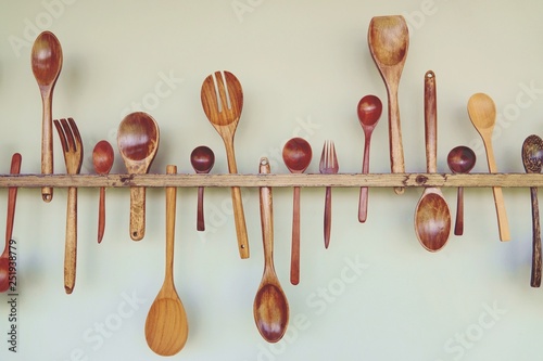 wooden kitchen tools: wooden spoon, wooden fork, wooden spatula, hang on white wall.