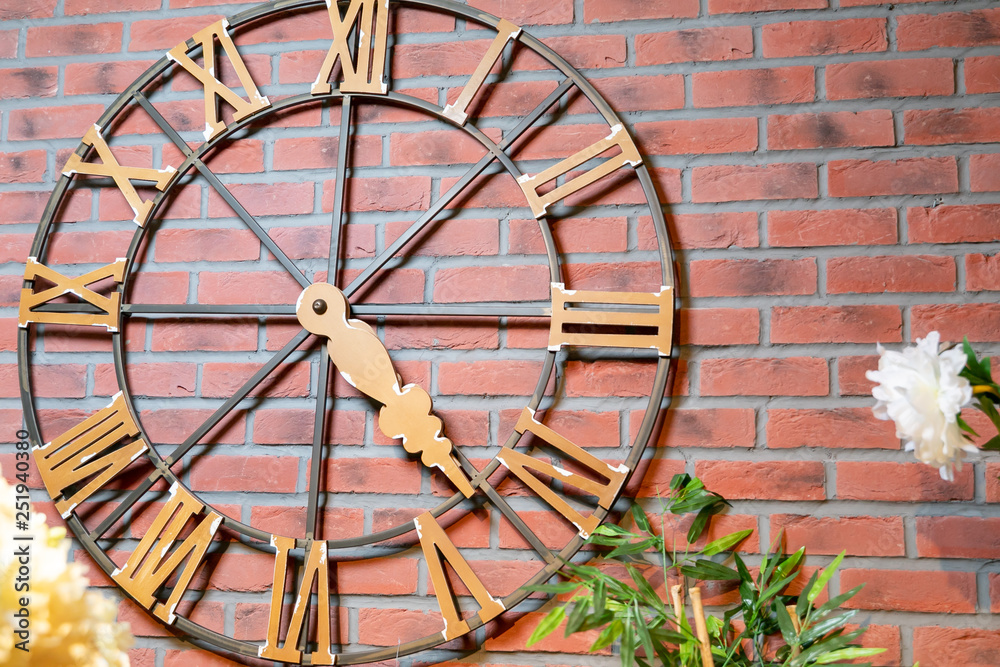 Brown, decorative clock with wooden figures hanging on a brown, brick wall.