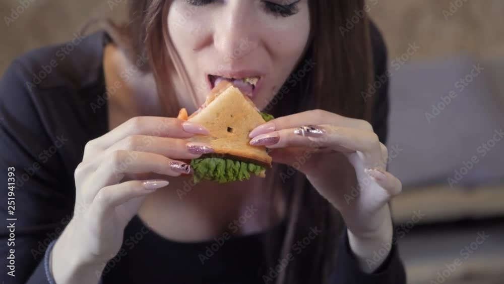 Sexy young girl eats sedvich. Close-up. The concept of quick snack and obesity society. Food for freelancer Sexy young girl eats sedvich. Close-up. The concept of quick snack and obesity society. Food for freelancer