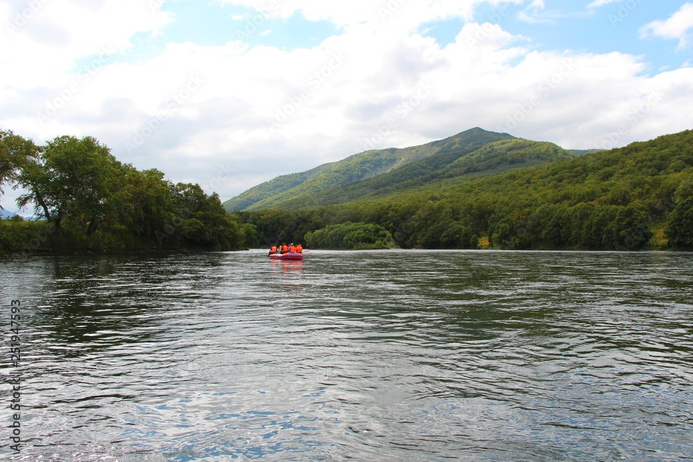 View of Bystraya Malkinskaya river on the Kamchatka Peninsula, Russia. Tourists on orange raft are visible on water.