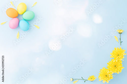 Colorful Easter eggs with springtime yellow flowers on a light blue background. Flat lay. Top view. Copy space