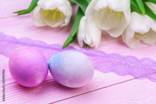 Easter background with colorful eggs and tulips over pink wood. Top view with copy space