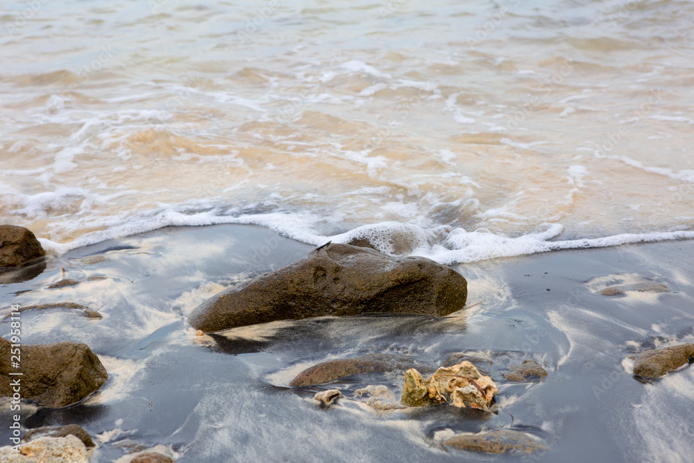 Fototapeta premium Lombok. Indonesia. The beach covered with volcanic ash. The sand near the shore is covered with a thin layer of volcanic ash, under it a fine yellow sand. Clear sea water.