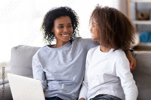 African mother and daughter sitting on couch using computer