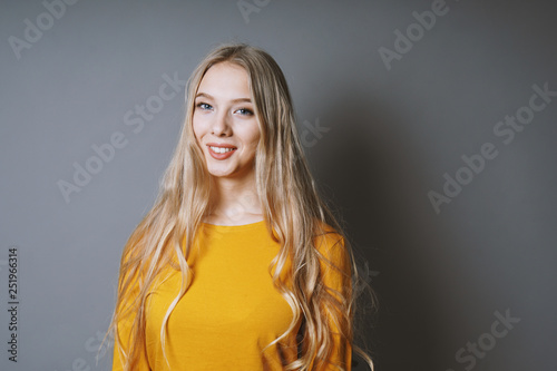 teenage girl with very long blond hair and beaming smile against gray background with copy space