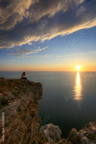 A woman photographs the sunset high above the sea on the rock Fiolent in Crimea