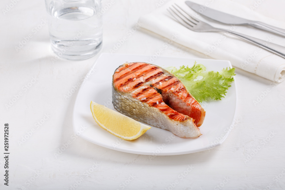 Grilled red salmon steak served with lemon and lettuce on white plate. Sockeye salmon, kokanee salmon or Oncorhynchus nerka.