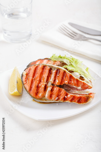 Grilled red salmon steak served with lemon and lettuce on white plate. Sockeye salmon, kokanee salmon or Oncorhynchus nerka.