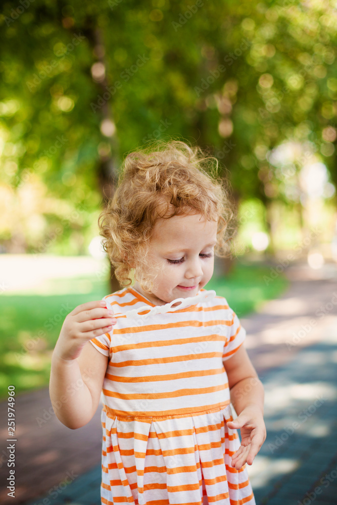 Little blonde curly girl blowing soap bubbles in summer park Little blonde curly girl blowing soap bubbles in summer park