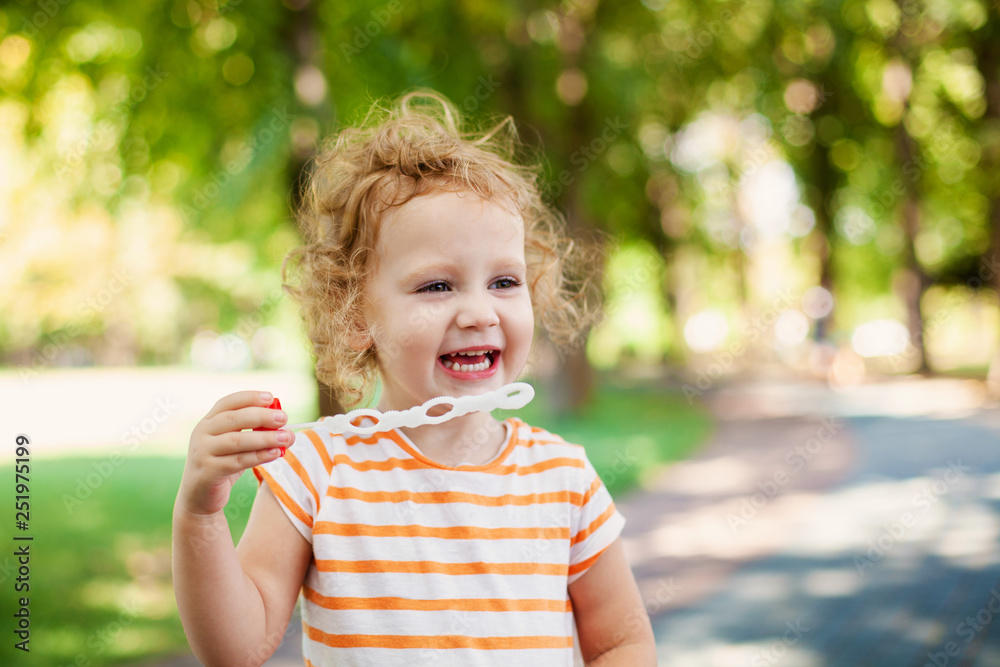 Little blonde curly girl blowing soap bubbles in summer park Little blonde curly girl blowing soap bubbles in summer park