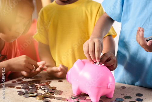 Group of asian children are helping putting coins into piggy bank on white background