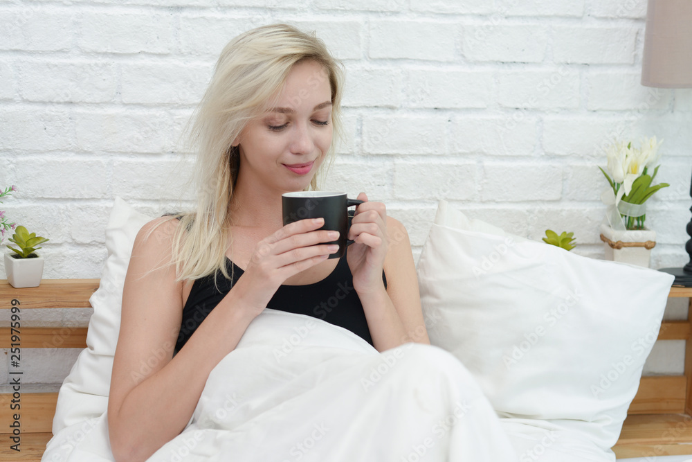Beautiful young smiling woman sitting on bed with a cup of coffee in the morning at bedroom. Beautiful young smiling woman sitting on bed with a cup of coffee in the morning at bedroom.