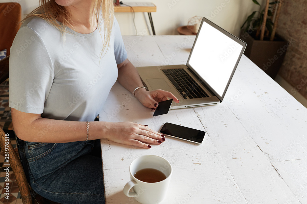 Fototapeta premium Pretty Woman using mobile phone and credit card for online shopping at home. Laptop on the table